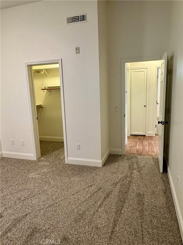 unfurnished bedroom with baseboards, visible vents, a walk in closet, carpet flooring, and a closet