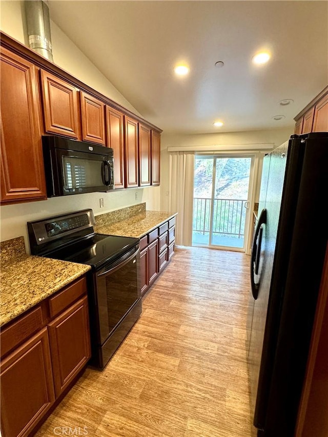 kitchen featuring black appliances, light wood-type flooring, light stone counters, and lofted ceiling