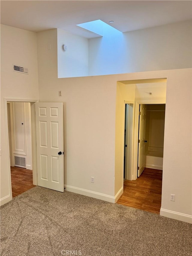 unfurnished room with carpet floors, a high ceiling, visible vents, and baseboards