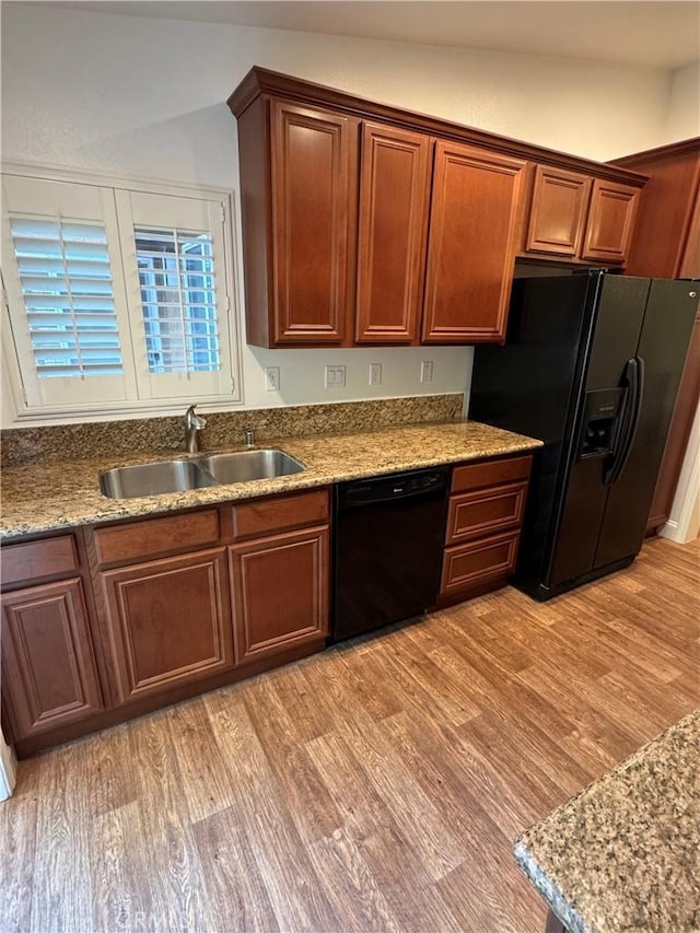 kitchen featuring light wood-style floors, a sink, light stone counters, and black appliances