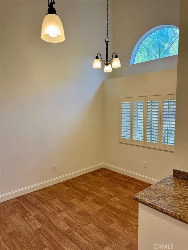 unfurnished dining area featuring an inviting chandelier, baseboards, and wood finished floors