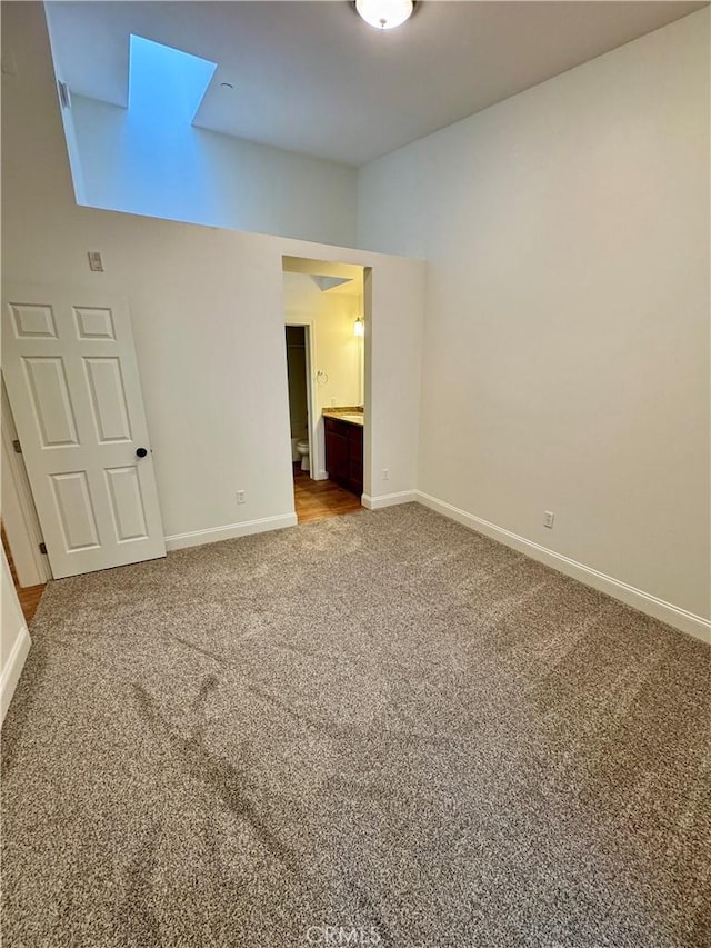 unfurnished bedroom with ensuite bath, a skylight, carpet flooring, and baseboards