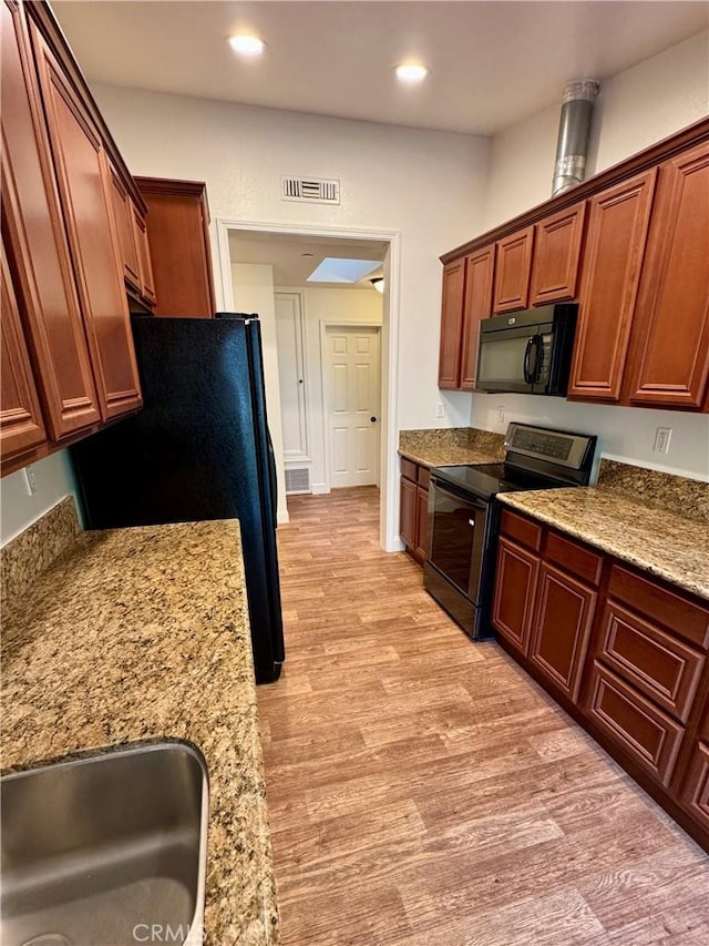 kitchen with light wood-type flooring, black appliances, visible vents, and light stone countertops