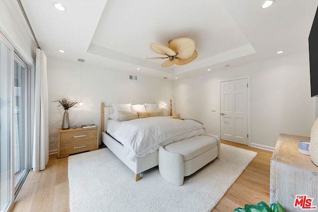 bedroom with multiple windows, a raised ceiling, light hardwood / wood-style flooring, and ceiling fan