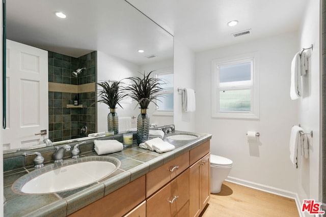 bathroom with a tile shower, hardwood / wood-style floors, vanity, and toilet