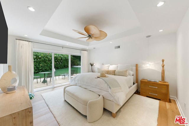 bedroom featuring ceiling fan, a raised ceiling, access to outside, and light hardwood / wood-style flooring