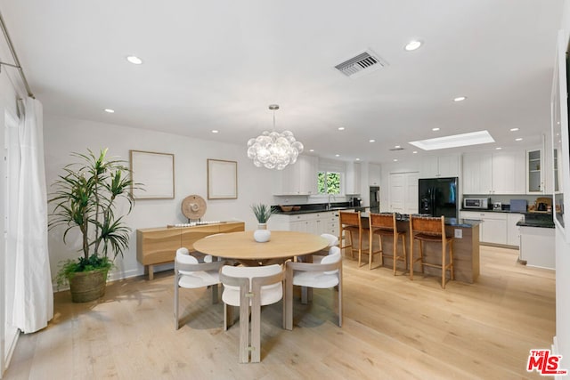 dining room featuring a skylight, light wood-type flooring, sink, and a chandelier