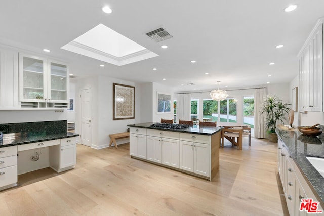 kitchen featuring decorative light fixtures, white cabinetry, light hardwood / wood-style flooring, and a skylight