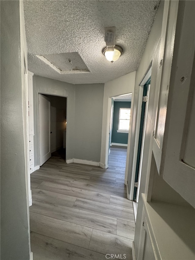 hall with light hardwood / wood-style floors and a textured ceiling