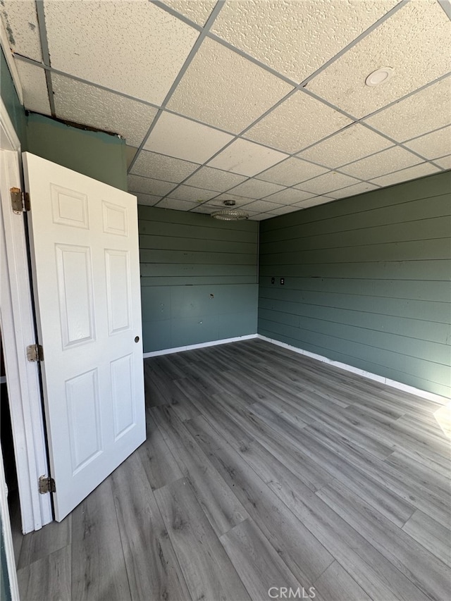 interior space featuring wood walls, hardwood / wood-style floors, and a drop ceiling