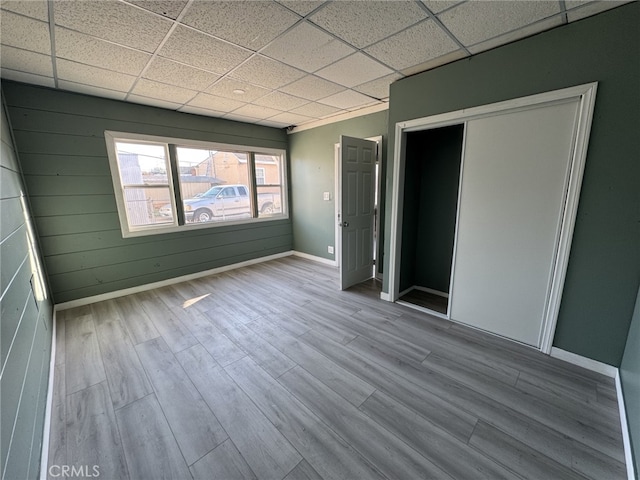 unfurnished room with a drop ceiling, wooden walls, and hardwood / wood-style flooring