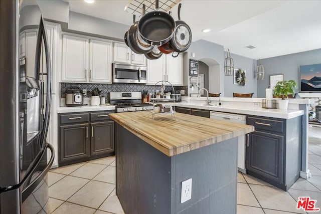 kitchen with white cabinetry, a center island, light tile patterned floors, kitchen peninsula, and stainless steel appliances