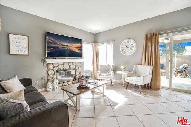 tiled living room with a stone fireplace and ceiling fan