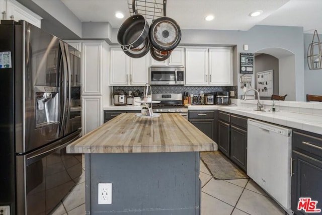 kitchen featuring light tile patterned floors, appliances with stainless steel finishes, a center island, white cabinets, and decorative backsplash