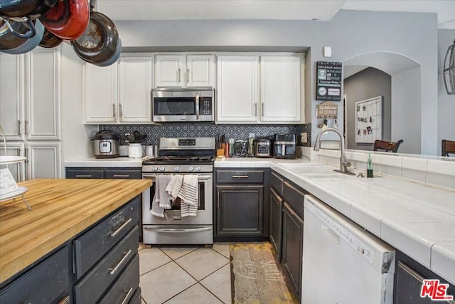 kitchen featuring sink, appliances with stainless steel finishes, tile counters, white cabinets, and decorative backsplash