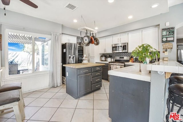 kitchen featuring backsplash, stainless steel appliances, a kitchen breakfast bar, white cabinets, and light tile patterned flooring