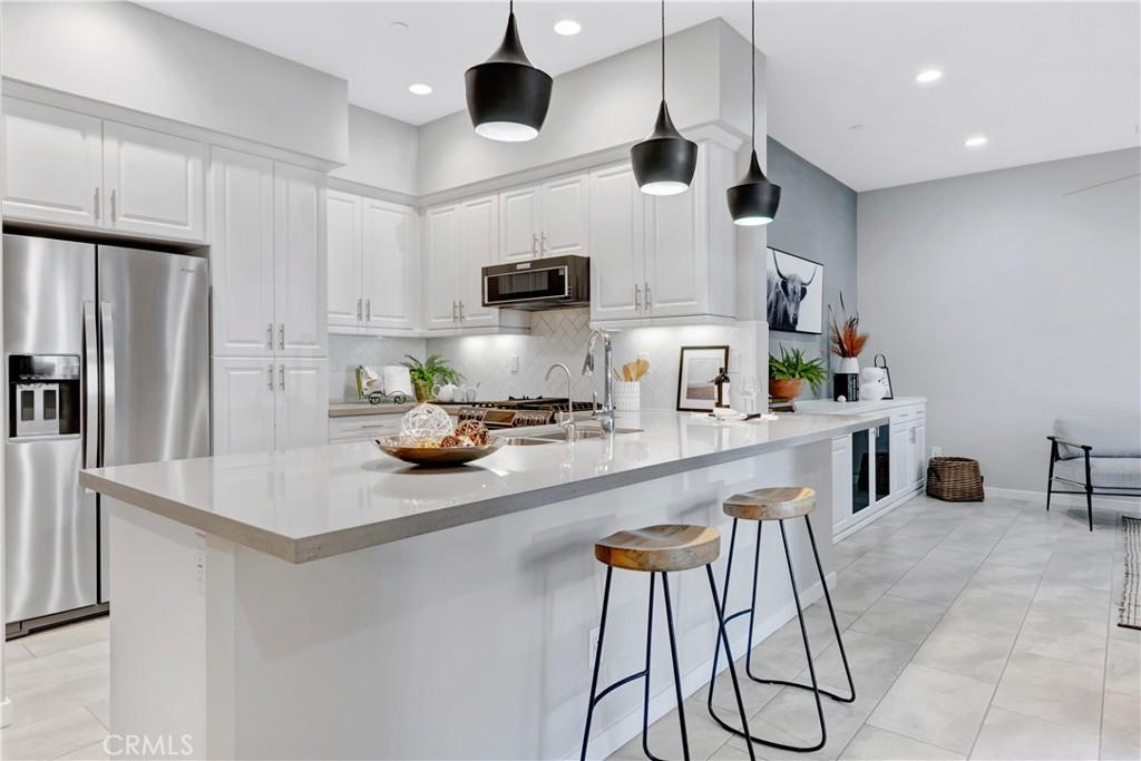 kitchen featuring stainless steel fridge, backsplash, light tile patterned floors, white cabinetry, and hanging light fixtures