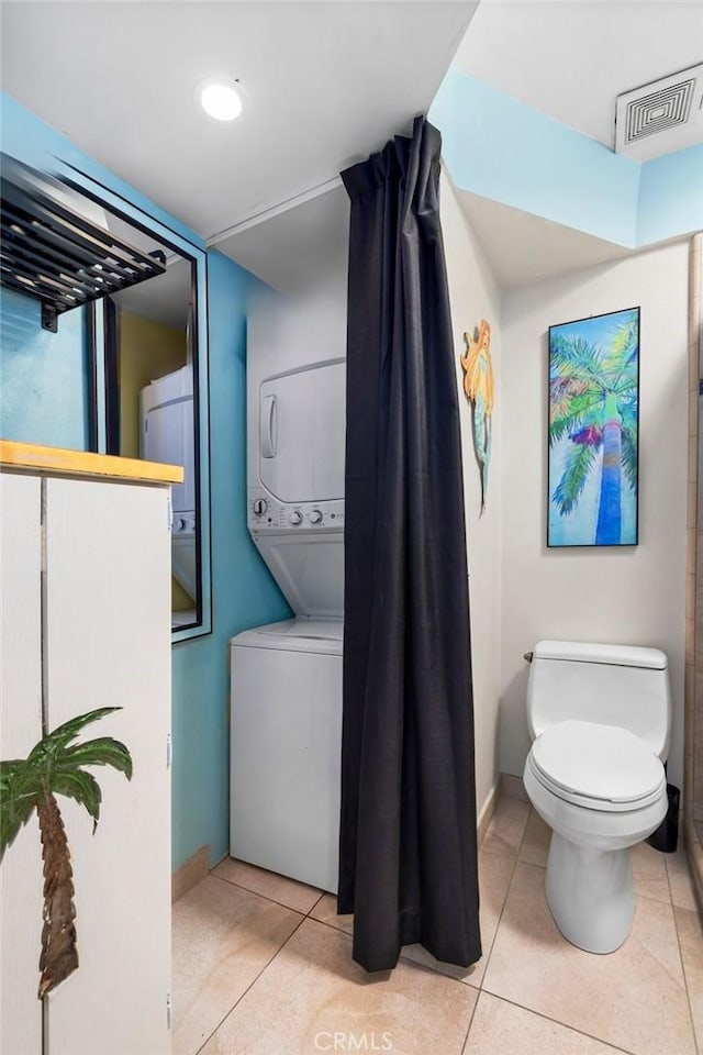 bathroom featuring tile patterned floors, stacked washer / dryer, and toilet