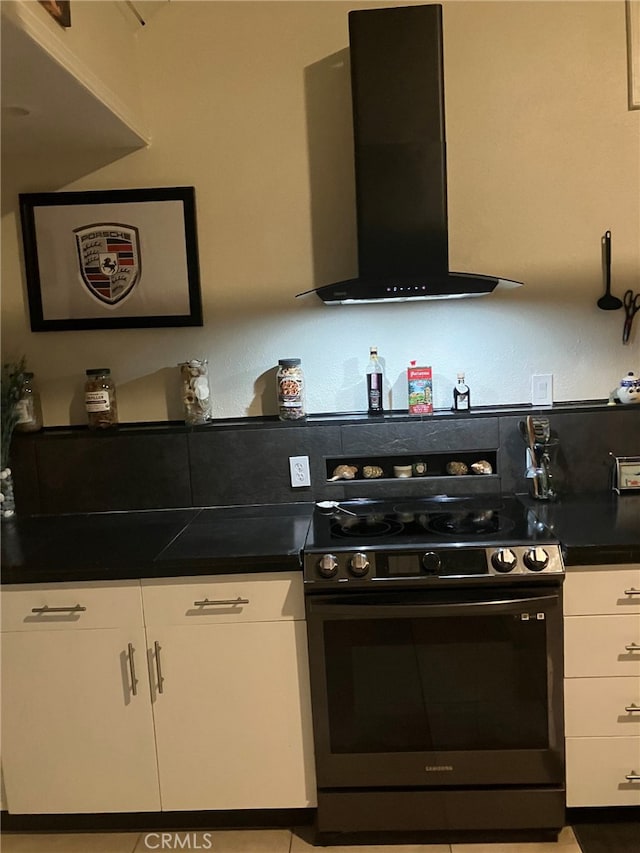 kitchen featuring white cabinetry, wall chimney range hood, light tile patterned flooring, and stove