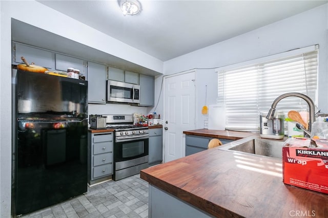 kitchen with gray cabinets, wood counters, sink, and stainless steel appliances