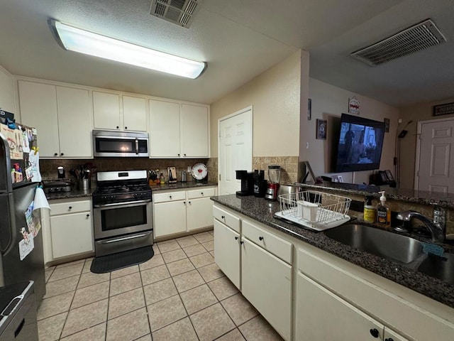 kitchen featuring appliances with stainless steel finishes, light tile patterned flooring, white cabinetry, backsplash, and sink