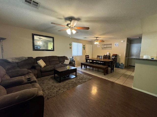 living room with ceiling fan, a textured ceiling, and light hardwood / wood-style flooring