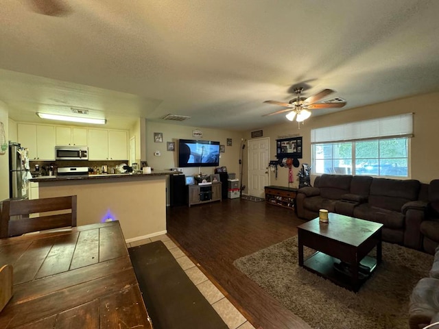 living room with ceiling fan, a textured ceiling, and light hardwood / wood-style floors