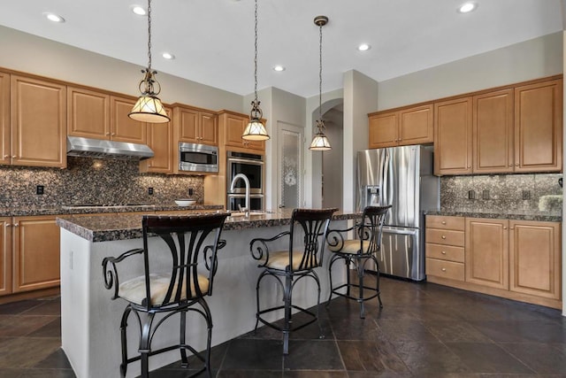 kitchen featuring a center island with sink, decorative backsplash, stainless steel appliances, and hanging light fixtures