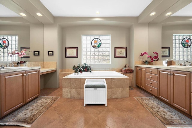 bathroom with tile patterned flooring, vanity, a wealth of natural light, and tiled bath