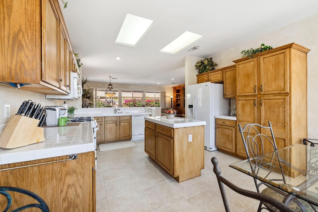 kitchen featuring a skylight, light tile patterned flooring, pendant lighting, white appliances, and a kitchen island