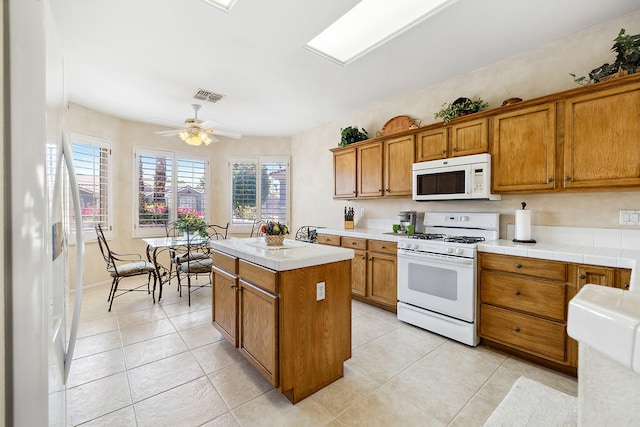 kitchen featuring ceiling fan, a center island, light tile patterned floors, and white appliances