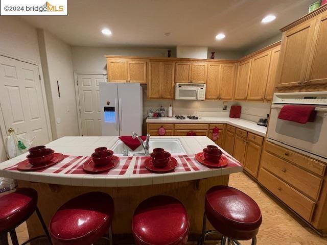 kitchen featuring tile countertops, a center island, white appliances, a breakfast bar, and sink