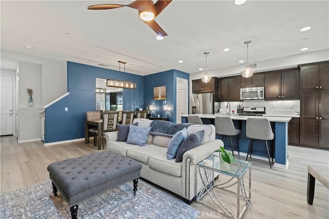 living room featuring ceiling fan, light wood-type flooring, and sink