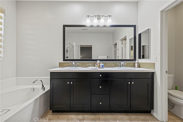 bathroom featuring tile patterned flooring, vanity, tiled bath, and toilet