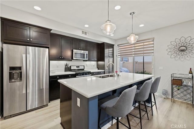 kitchen with dark brown cabinets, stainless steel appliances, sink, a center island with sink, and hanging light fixtures