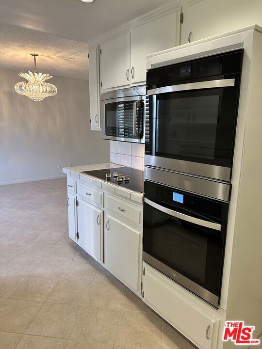 kitchen with pendant lighting, white cabinets, a textured ceiling, appliances with stainless steel finishes, and a notable chandelier