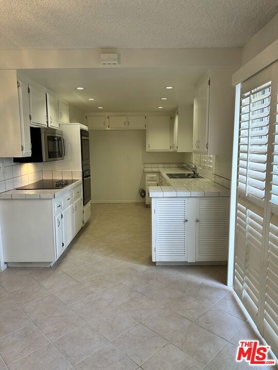 kitchen featuring tile countertops, backsplash, black appliances, sink, and white cabinetry