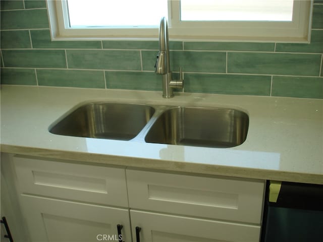 room details featuring backsplash, sink, light stone counters, and white cabinetry