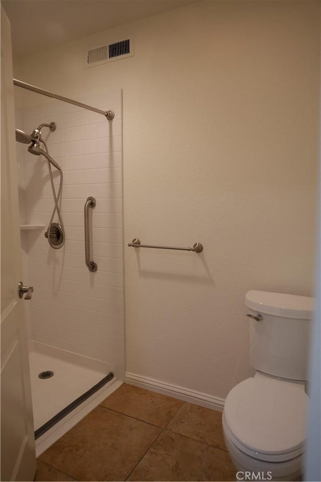 bathroom featuring toilet, tile patterned flooring, and a tile shower