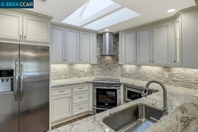 kitchen with a skylight, light stone counters, stainless steel appliances, and wall chimney range hood