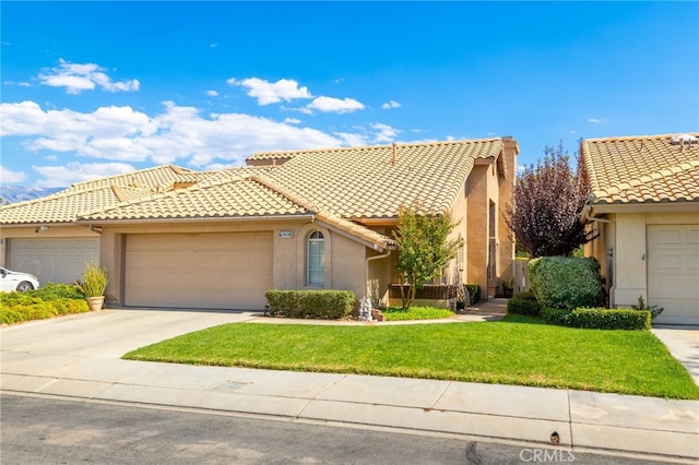 mediterranean / spanish-style house featuring a tiled roof, an attached garage, concrete driveway, a front lawn, and stucco siding