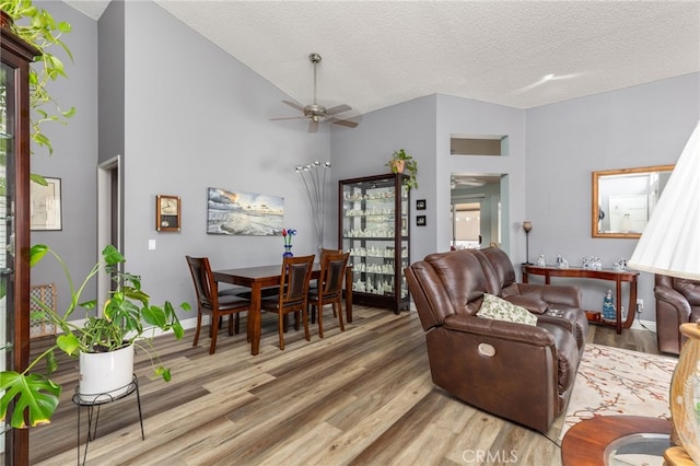 living room with high vaulted ceiling, wood-type flooring, ceiling fan, and a textured ceiling