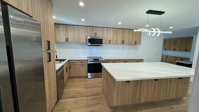 kitchen with stainless steel appliances, decorative backsplash, light brown cabinets, decorative light fixtures, and a center island