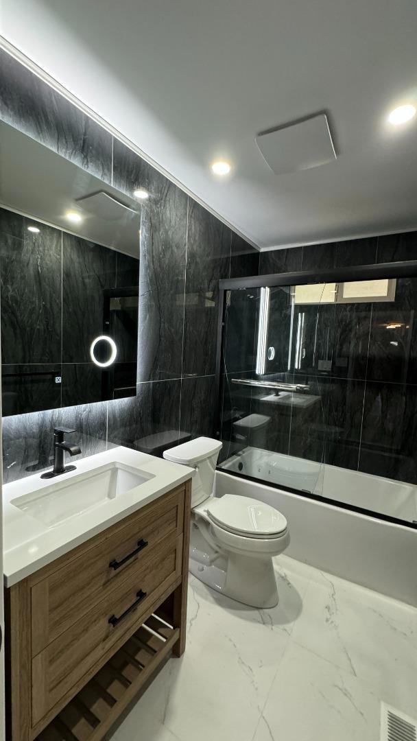 full bathroom featuring combined bath / shower with glass door, vanity, tile walls, and toilet