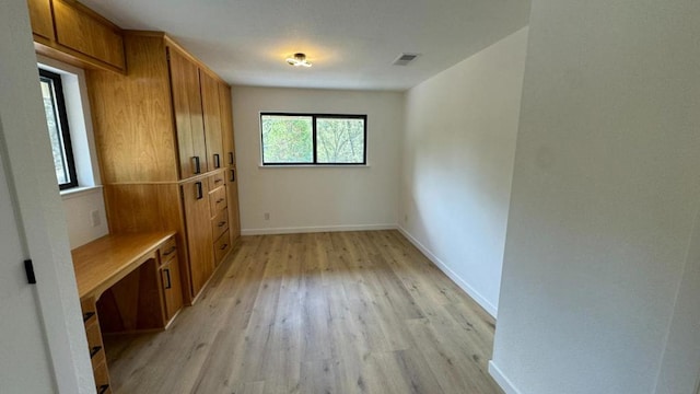 spare room featuring built in desk and light hardwood / wood-style floors