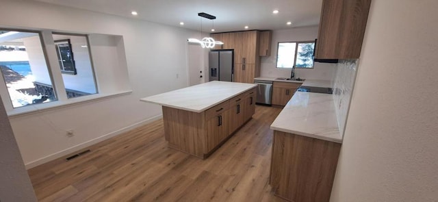 kitchen featuring stainless steel appliances, decorative backsplash, a center island, hanging light fixtures, and sink