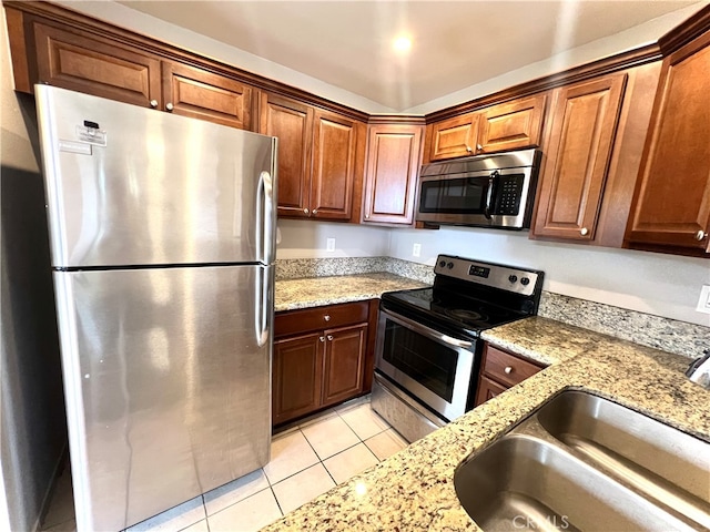 kitchen with appliances with stainless steel finishes, light stone countertops, sink, and light tile patterned flooring