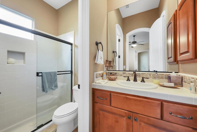 bathroom with backsplash, a shower with shower door, ceiling fan, vanity, and toilet