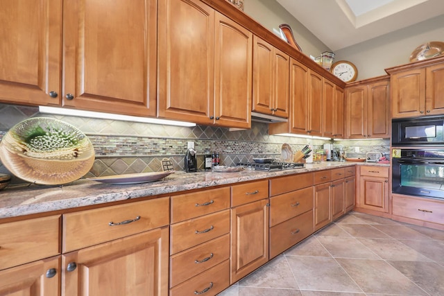 kitchen with light stone counters, vaulted ceiling, black appliances, backsplash, and light tile patterned floors