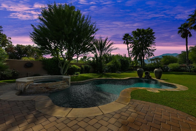 pool at dusk with a lawn, an in ground hot tub, and a patio area